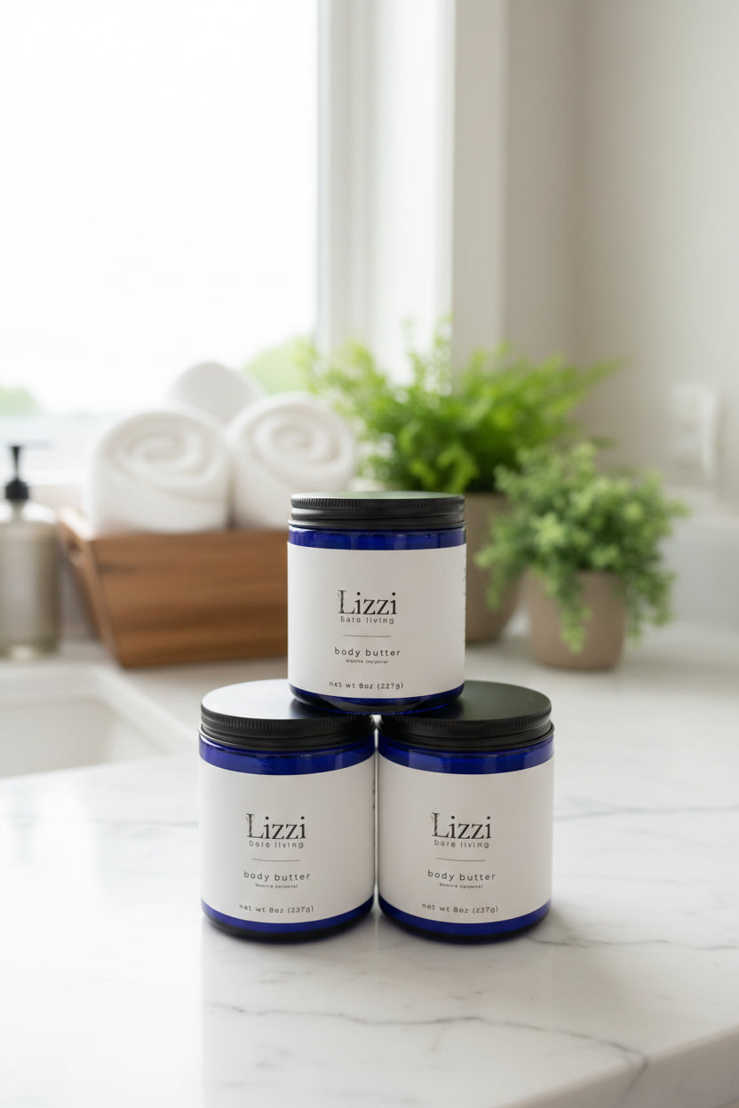 Three blue glass containers of Lizzi bare living body butter with black lids on a clean bathroom backdrop